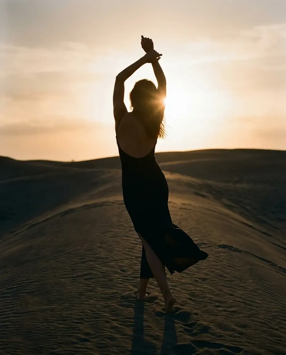 Frau im schwarzen Kleid tanzt bei Sonnenuntergang auf einer Sanddüne