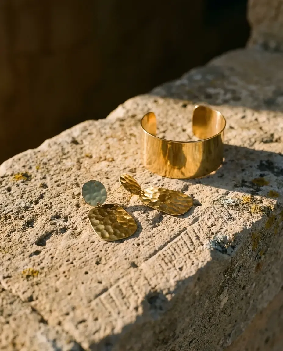 Goldener Armreif und gehämmerte Ohrringe auf einem Stein in der Abendsonne